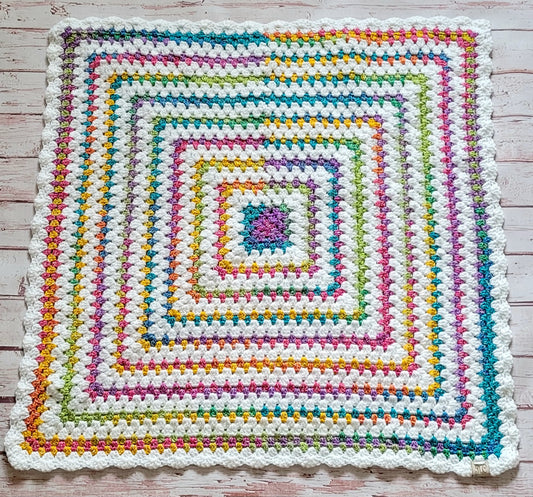 One-of-a-kind 30x30 hand crocheted baby and lap blanket with colorful Rainbow cotton accents, white scalloped border, and Johanna Lesley Creations tag.
